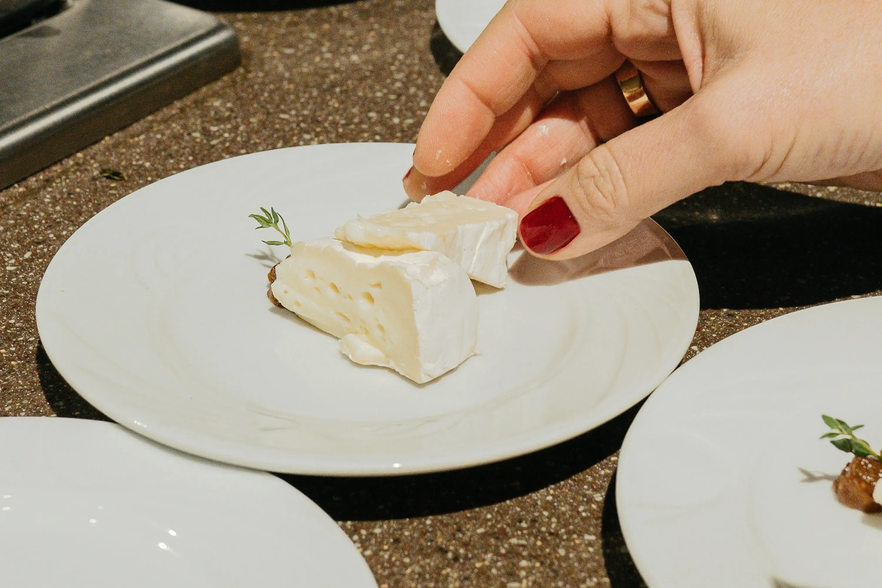 hand reaching for a piece of cheese on a white plate